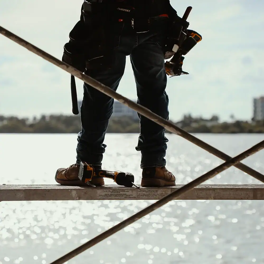 someone standing on a scaffold with a drill on the ground and a construction belt around his waist