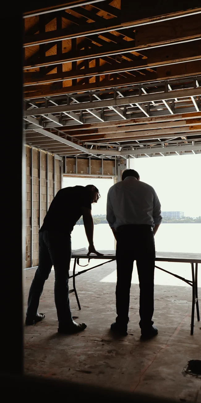 picture of tow men in the base frames of a home standing over a table over looking water