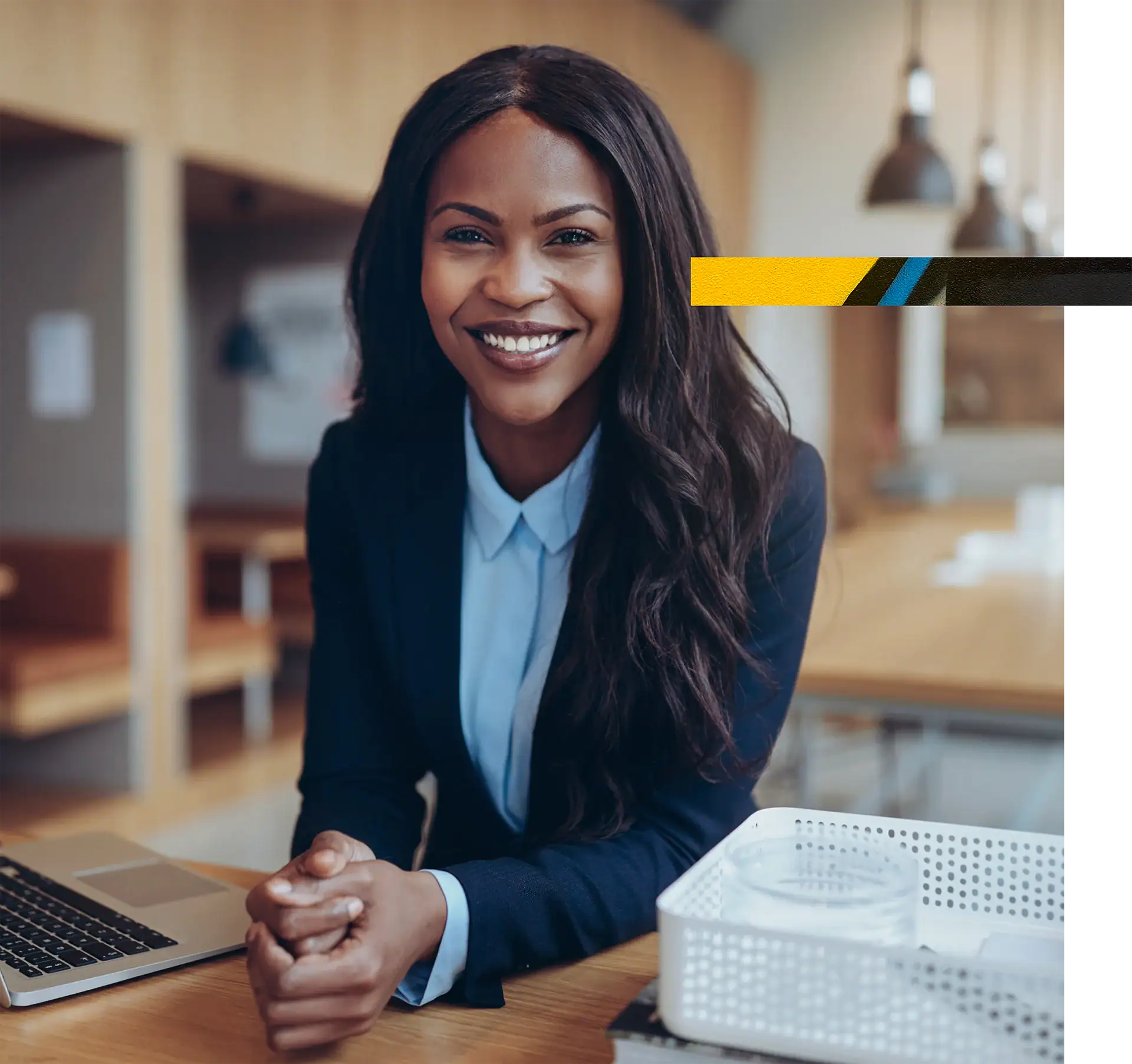 Professional woman smiling, sitting at her desk with a laptop and office supplies.