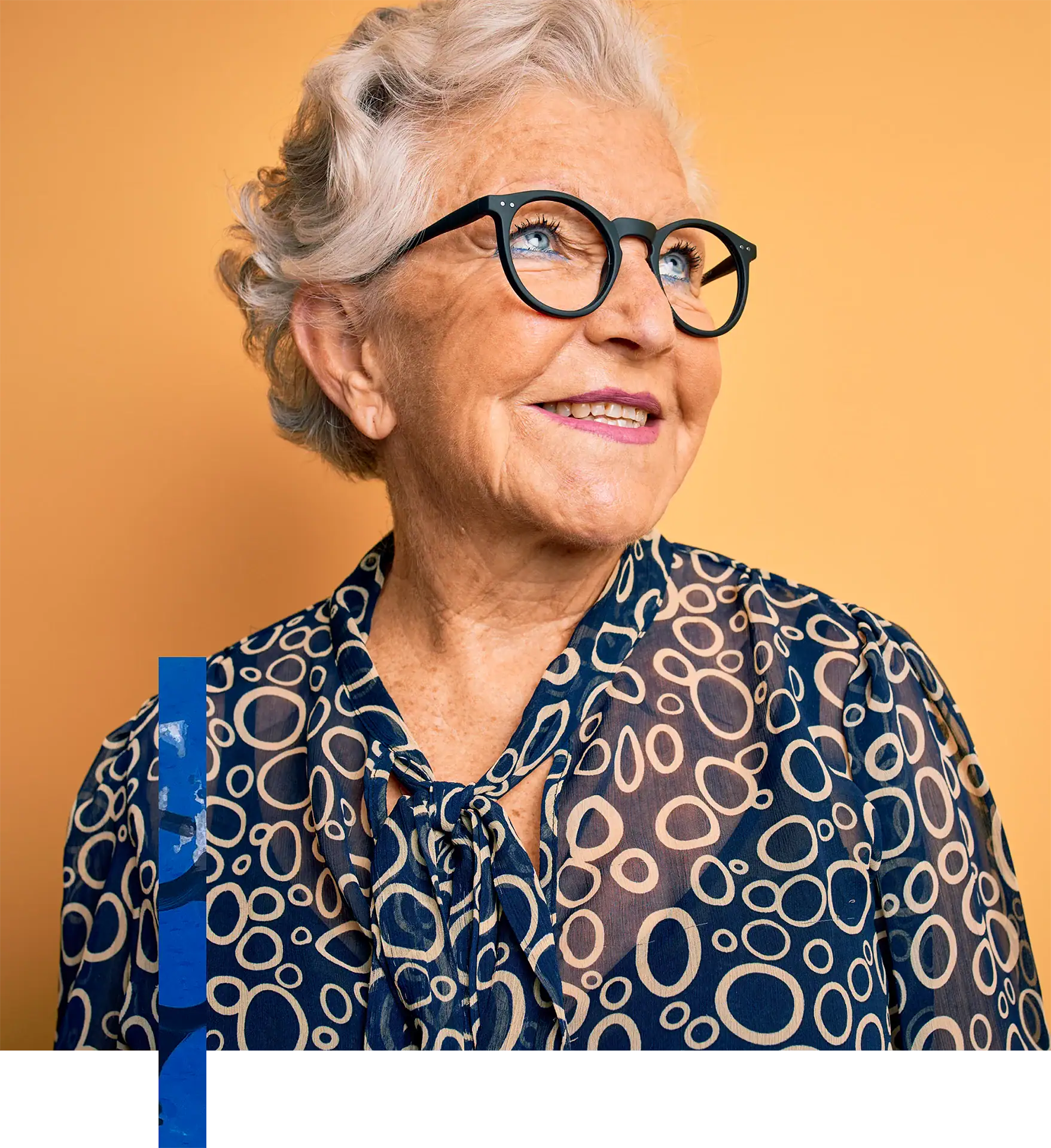 Elegant elderly woman with short gray hair, black glasses, and a stylish patterned blouse, smiling h.