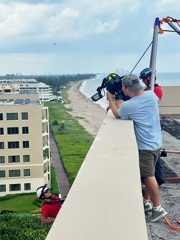Film Crew Capturing Man with Sunglasses and a Helmet Scaling a building