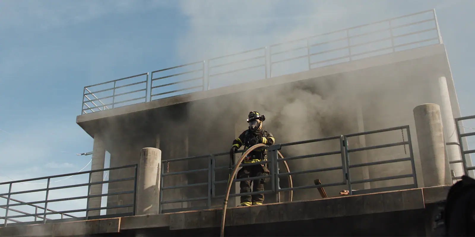 fire fighter standing on a ledge with smoke the building in the background