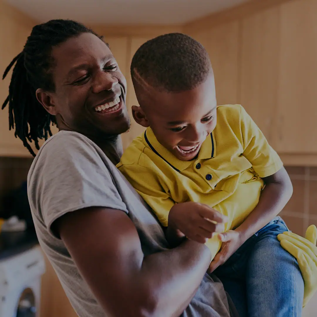 Picture of a father and son playing together laughing while the dad holds up the kid