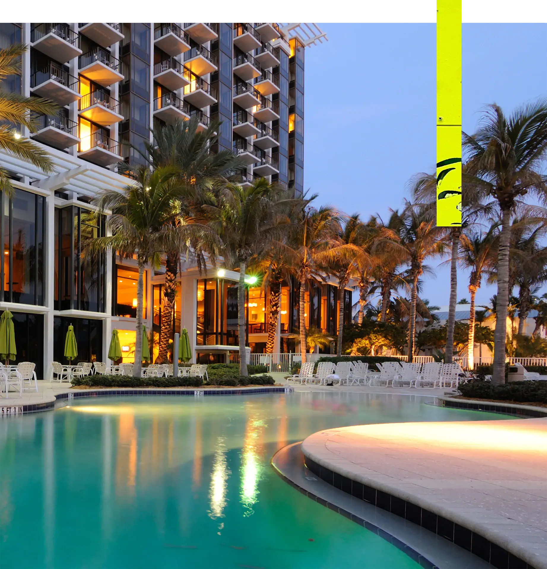 Elegant hotel pool surrounded by palm trees and outdoor seating at sunset.