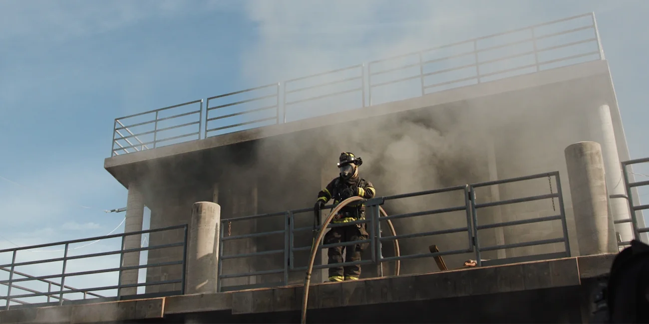 fire fighter standing on a ledge with smoke the building in the background