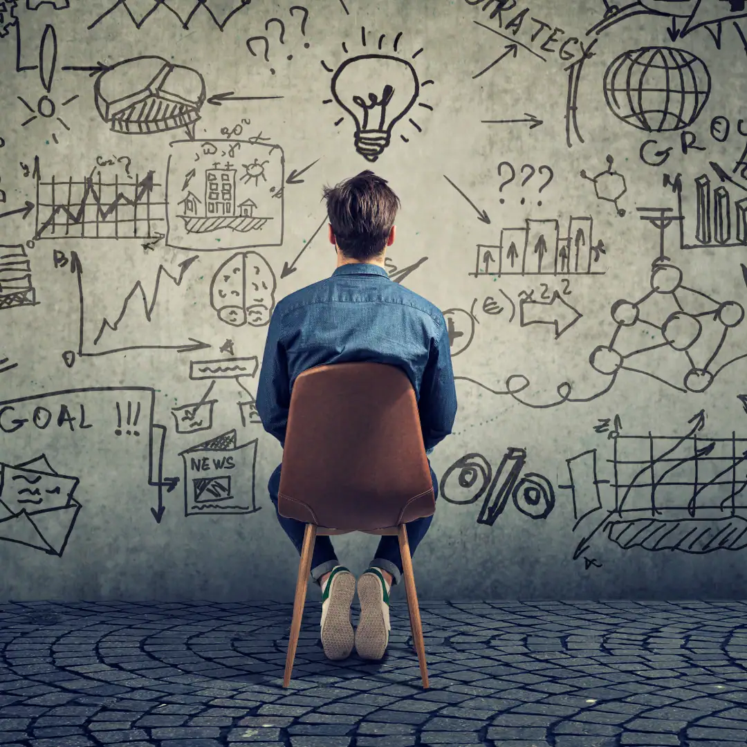 Man sitting in a chair facing a wall with a variety of doodles on the wall